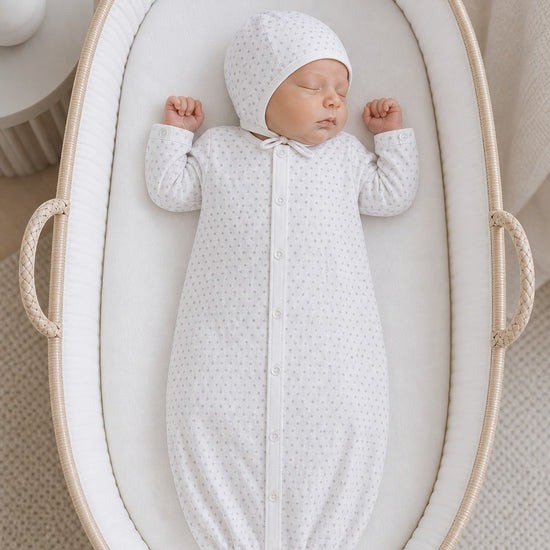 Carriage Boutique infant sleep gown and matching bonnet in white with grey star print, worn by a sleeping newborn.