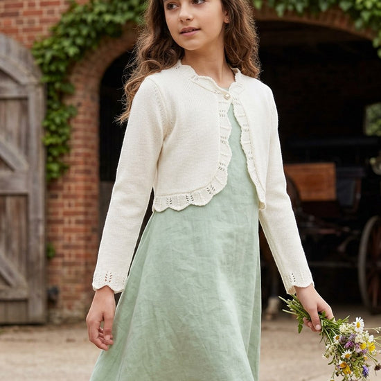 Carriage Boutique ivory cotton bolero shrug sweater with scalloped edges worn by a girl in a green dress