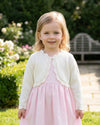 Carriage Boutique toddler girl wearing an ivory cotton bolero shrug with scalloped edges over a light pink dress