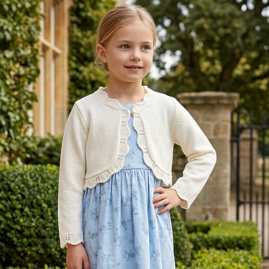 Carriage Boutique ivory cotton bolero shrug sweater with scalloped edges worn by a young girl over a blue floral dress