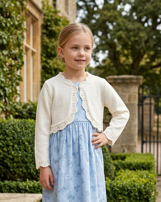 Carriage Boutique ivory cotton bolero shrug sweater with scalloped edges worn by a young girl over a blue floral dress