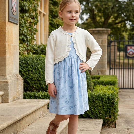 Carriage Boutique ivory cotton bolero shrug worn by a young girl over a blue floral dress outdoors