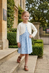 Carriage Boutique ivory cotton bolero shrug worn by a young girl over a blue floral dress outdoors