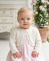 Carriage Boutique ivory cotton bolero shrug with delicate scalloped edges worn by a baby girl over a pink dress.