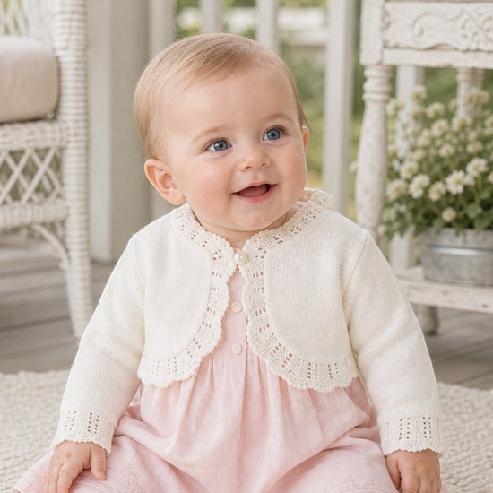 Carriage Boutique ivory cotton bolero shrug sweater with delicate knit detailing worn by a smiling baby girl