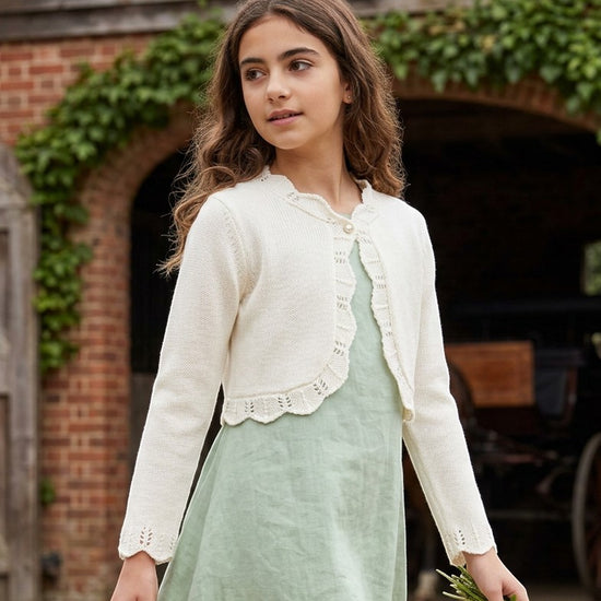 Carriage Boutique ivory cotton bolero shrug sweater with delicate scalloped edges worn by a girl in a green dress