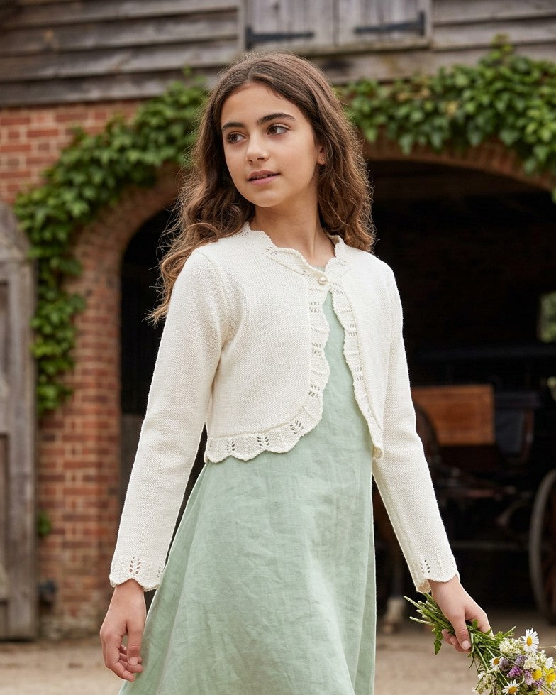 Carriage Boutique ivory cotton bolero shrug sweater with delicate scalloped edges worn by a girl in a green dress