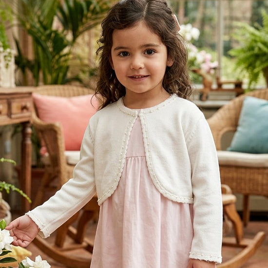 Carriage Boutique ivory knit bolero sweater with pearl trim worn by a toddler girl over a light pink dress