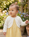 Carriage Boutique ivory knit bolero sweater with delicate pearl trim worn by a baby girl in a garden setting