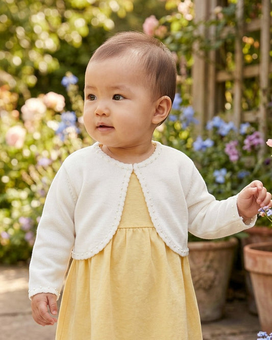 Carriage Boutique ivory knit bolero sweater with delicate pearl trim worn by a baby girl in a garden setting