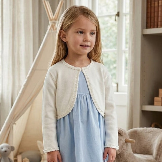 Carriage Boutique ivory knit bolero sweater with pearl trim worn by a young girl over a light blue dress.