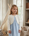 Carriage Boutique ivory knit bolero sweater with pearl trim worn by a young girl over a light blue dress.