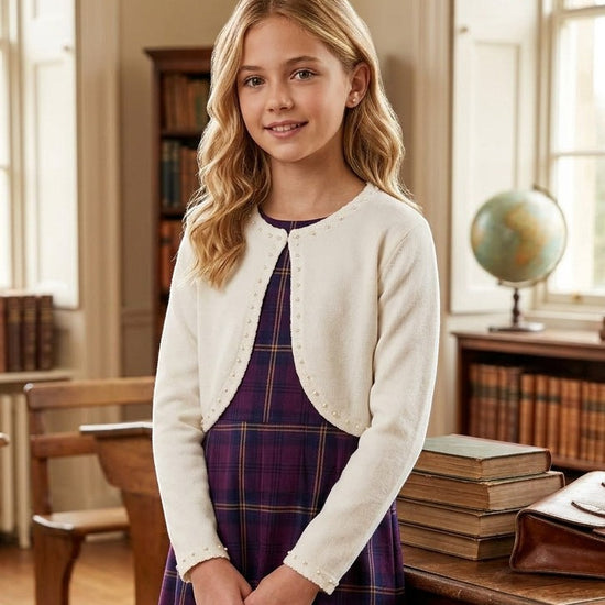 Carriage Boutique ivory knit bolero sweater with pearl trim worn by a young girl over a purple plaid dress