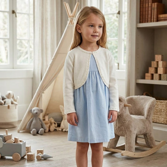Carriage Boutique ivory knit bolero sweater worn by a young girl over a light blue dress in a nursery setting