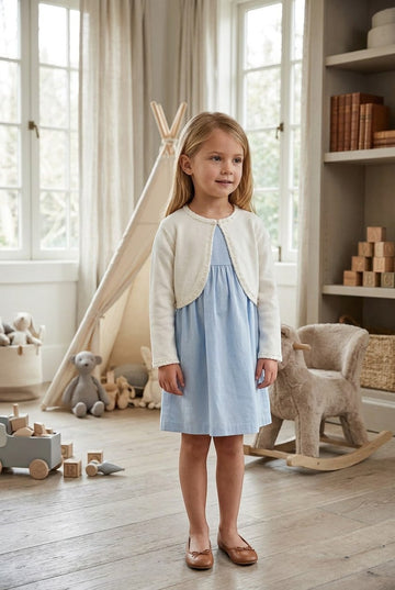 Carriage Boutique ivory knit bolero sweater worn by a young girl over a light blue dress in a nursery setting