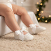 Carriage Boutique ivory lace baptism shoes with satin ribbon bows worn by a baby girl on a soft carpet