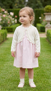 Carriage Boutique toddler girl wearing an ivory cotton bolero shrug with delicate scalloped edges over a pink dress