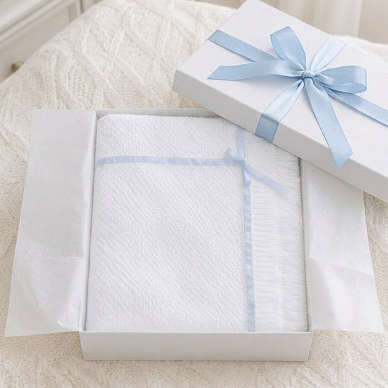 Carriage Boutique Julius Berger white knit baby blanket with blue satin ribbon trim inside a gift box