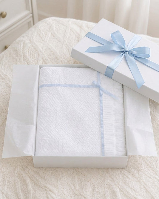 Carriage Boutique Julius Berger white knit baby blanket with blue satin ribbon trim inside a gift box