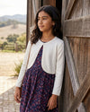 Carriage Boutique Julius Berger white bolero sweater worn by a young girl over a floral dress by a rustic barn door.