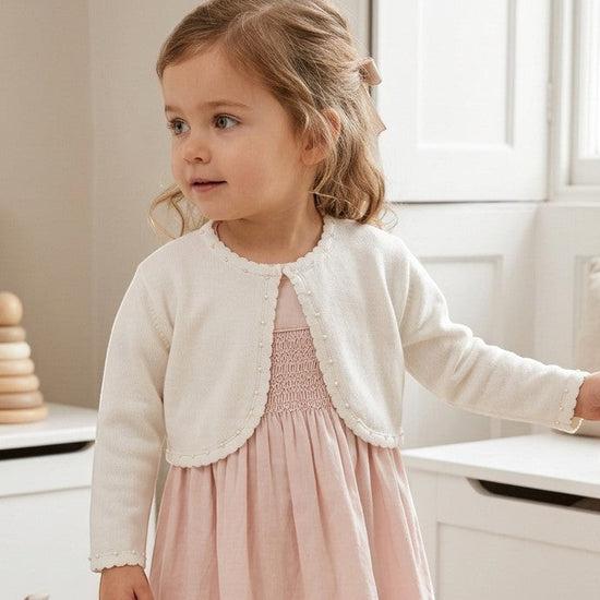 Carriage Boutique toddler girl wearing a white Julius Berger bolero sweater with pearl trim over a pink dress