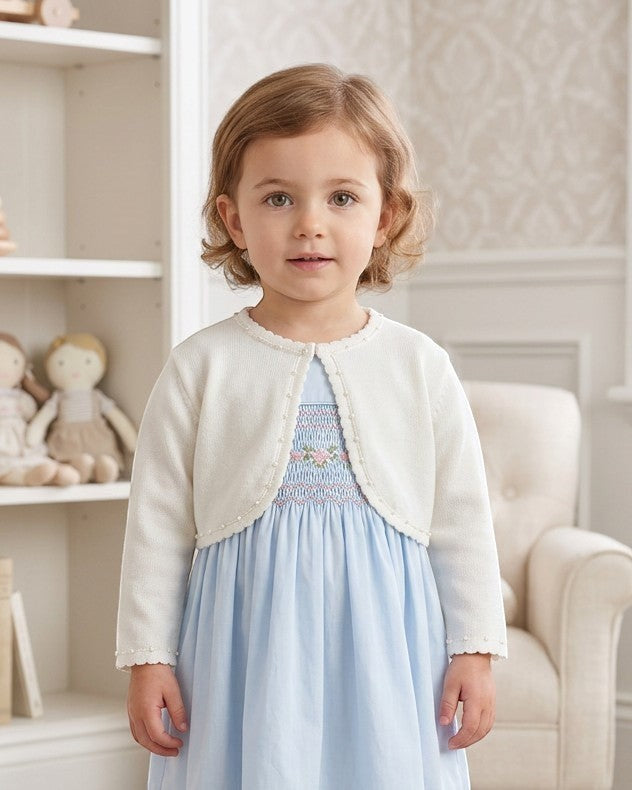 Carriage Boutique toddler girl wearing a white Julius Berger bolero sweater over a light blue smocked dress.