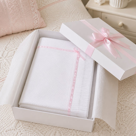 Carriage Boutique Julius Berger white knit baby blanket with pink satin ribbon trim inside a gift box