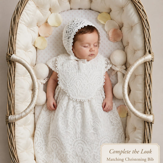 Carriage Boutique white lace christening gown and matching bonnet worn by a sleeping baby in a wicker bassinet.