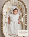 Carriage Boutique white lace christening gown and matching bonnet worn by a sleeping baby in a wicker bassinet.