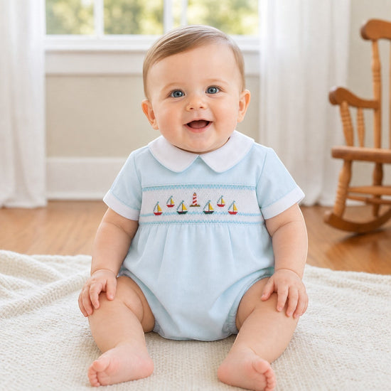 Carriage Boutique light blue smocked bubble romper with sailboat embroidery and white collar, on a baby.