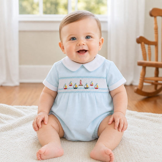 Carriage Boutique light blue smocked bubble romper with sailboat embroidery and white collar, on a baby.