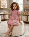 Carriage Boutique mauve suede-like baby dress with smocked embroidered yoke and short sleeves worn by a young girl