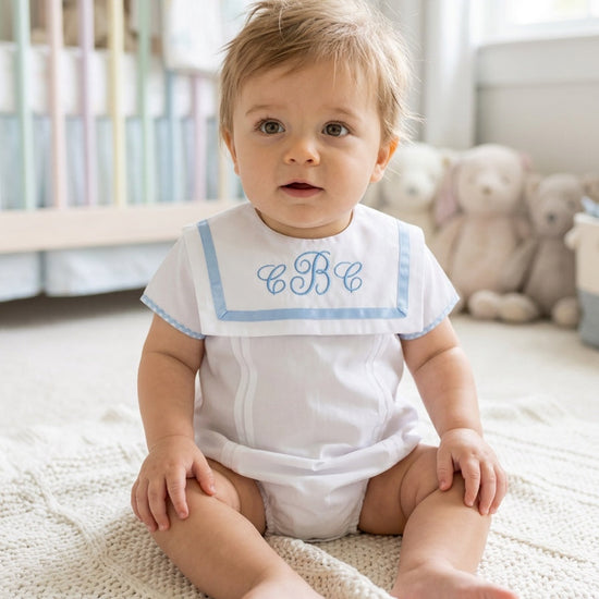 Carriage Boutique baby boy white bubble romper with blue trim, Peter Pan collar, and custom monogram in a nursery.
