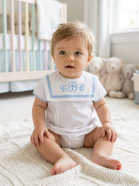 Carriage Boutique baby boy white bubble romper with blue trim, Peter Pan collar, and custom monogram in a nursery.