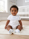Carriage Boutique baby boy wearing a white bubble romper with a blue monogrammed collar, sitting on a knit blanket.