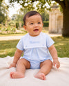 Carriage Boutique baby boy wearing a light blue cotton bubble romper with a white monogrammed bib sitting on a blanket