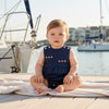 Carriage Boutique navy blue sleeveless baby romper with embroidered sailboats and red & white sails. Features shoulder buttons and snap closure.