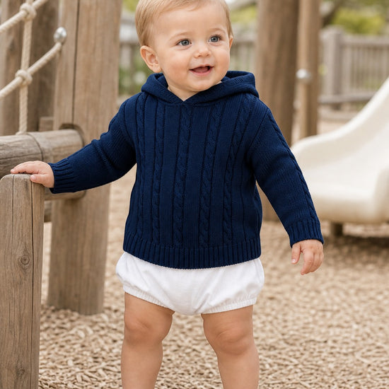 Carriage Boutique navy cable knit baby hooded sweater worn by a toddler at a playground