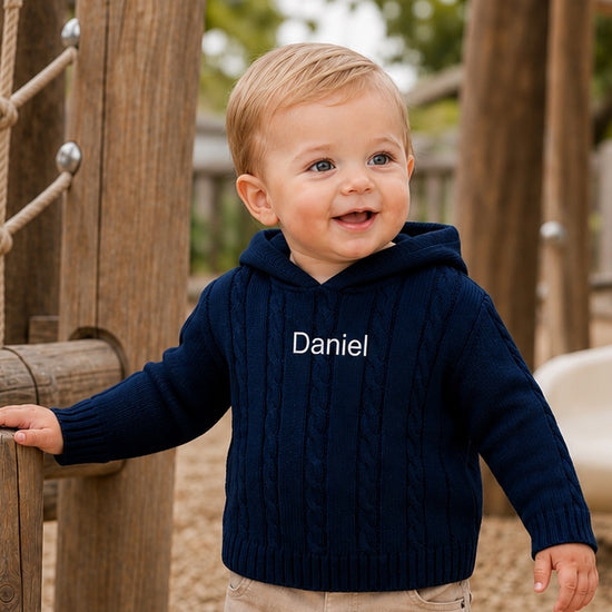 Carriage Boutique navy cable knit baby sweater with hood and custom Daniel embroidery on chest worn by a toddler