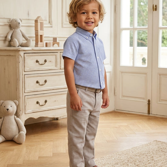 Carriage Boutique toddler boy wearing a navy blue check short-sleeve polo shirt with beige trousers and loafers.