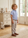 Carriage Boutique toddler boy wearing a navy blue check short-sleeve polo shirt with beige trousers and loafers.