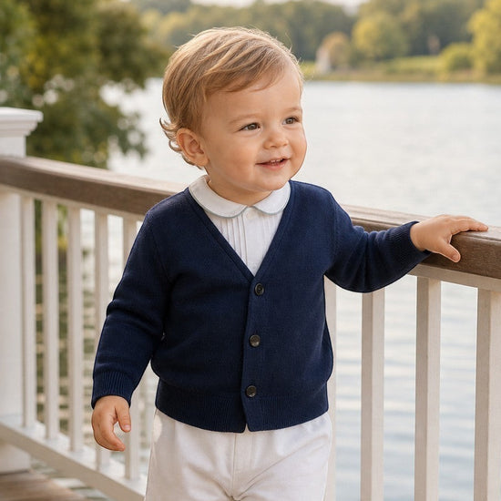 Toddler boy wearing a Carriage Boutique navy blue V-neck cotton cardigan over a white collared shirt by a lake.