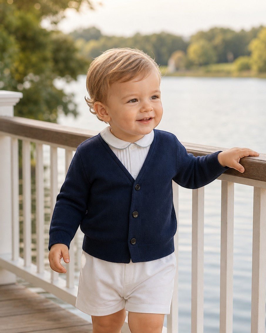 Toddler boy wearing a Carriage Boutique navy blue V-neck cotton cardigan over a white collared shirt by a lake.
