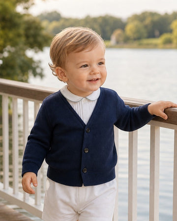 Toddler boy wearing a Carriage Boutique navy blue V-neck cotton cardigan over a white collared shirt by a lake.