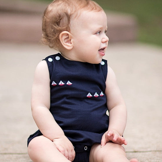 Carriage Boutique navy blue sleeveless baby romper with embroidered sailboats and white shoulder buttons.