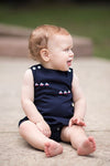 Carriage Boutique navy blue sleeveless baby romper with embroidered sailboats and white shoulder buttons.