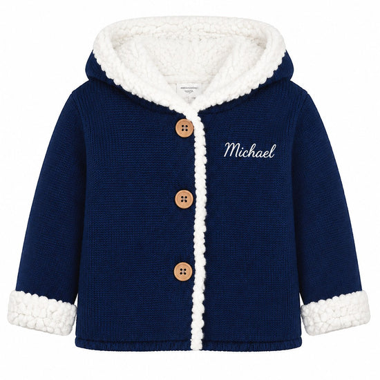 Carriage Boutique navy knit cotton baby jacket with white sherpa lining, hood, and wooden buttons.