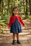 Carriage Boutique navy silk floral smocked dress with a red cardigan worn by a young girl on a forest path