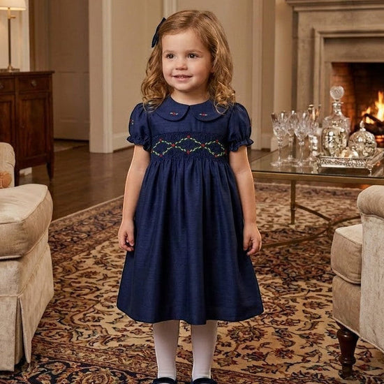 Carriage Boutique navy silk toddler party dress with smocked floral collar and puffy sleeves in a living room.