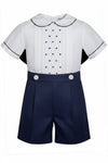 Carriage Boutique navy tucks with dots baby boy suit. White short-sleeve shirt with pintucks, navy dots, Peter Pan collar, and navy piping. Navy shorts with pleats and white buttons.